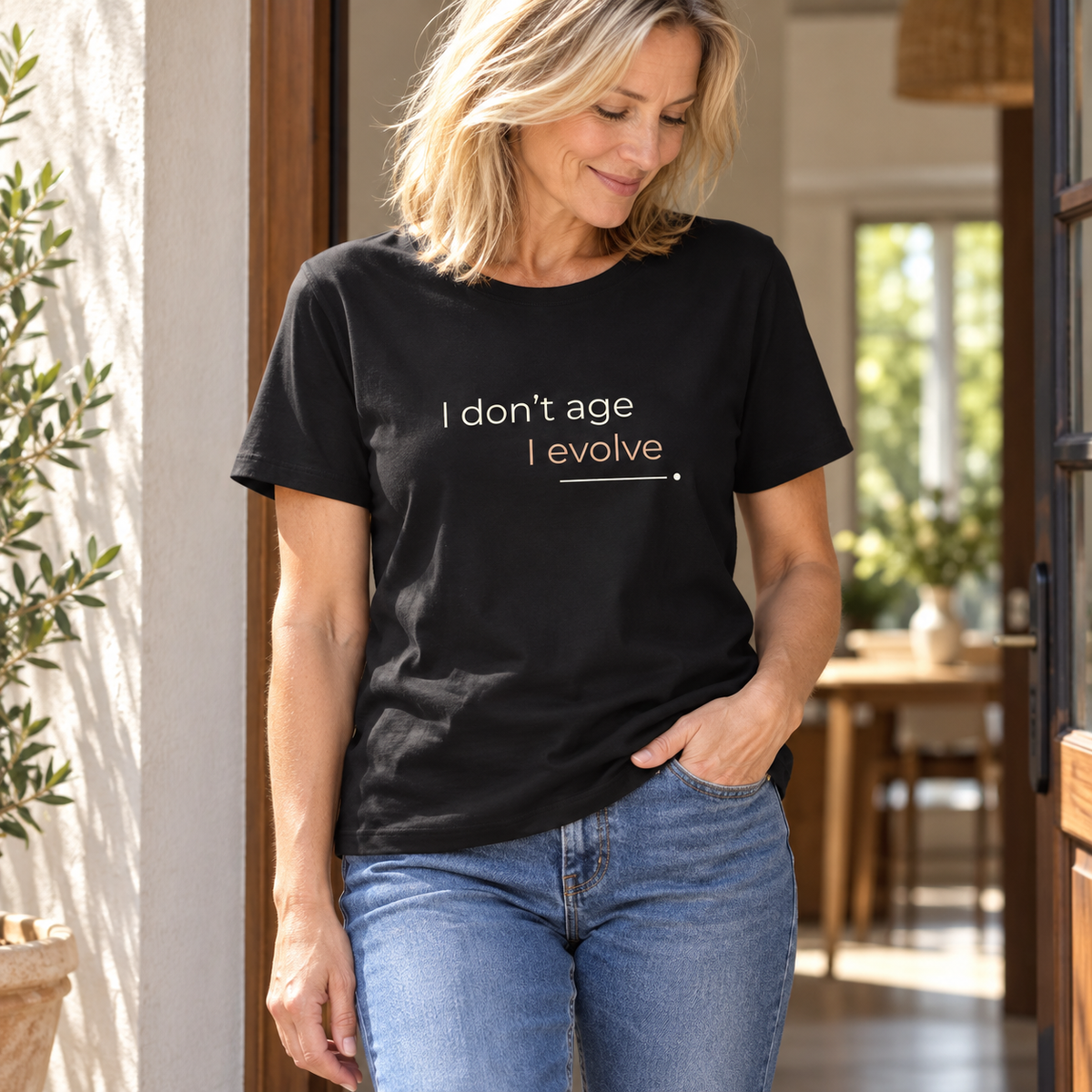 Mulher com T-shirt preta «I don't age, I evolve» e jeans, num interior luminoso.