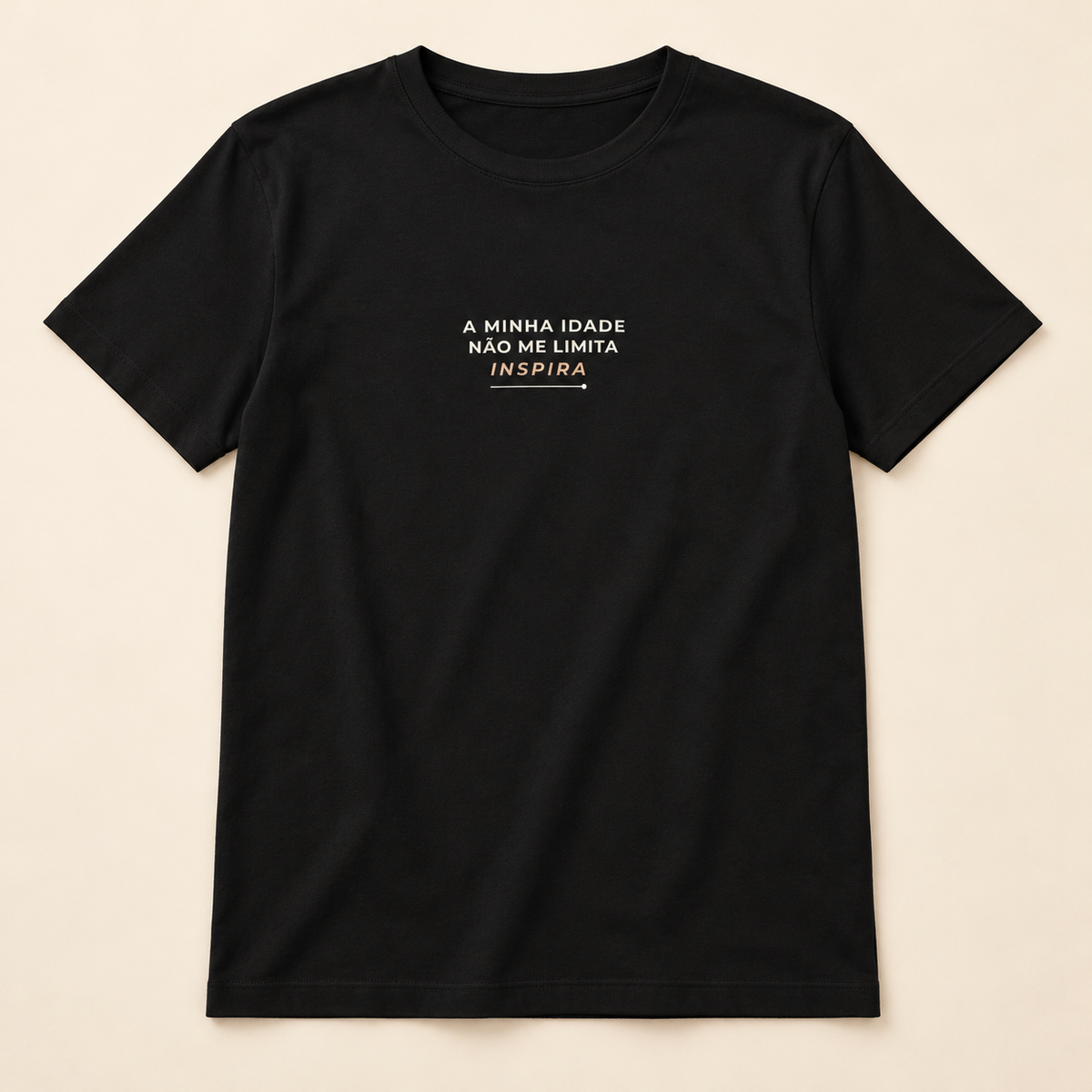 T-shirt preta «A minha idade não me limita, inspira», vista de frente sobre fundo creme.