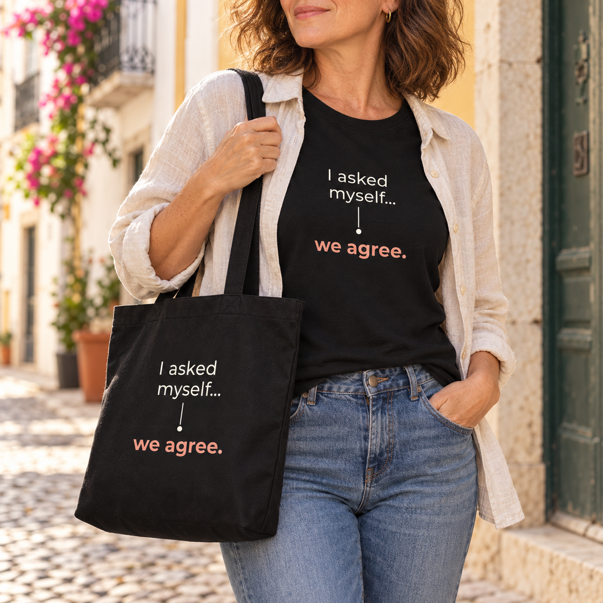 Mulher com t-shirt e tote bag pretas “I asked myself... we agree.”, camisa clara e jeans numa rua; imagem gerada com estética UGC.