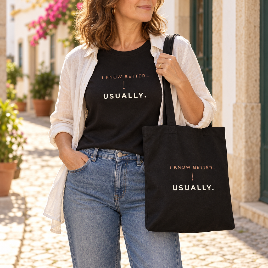 Mulher com t-shirt e tote bag pretas “I know better... usually.”, camisa clara e jeans numa rua; imagem gerada com estética UGC.