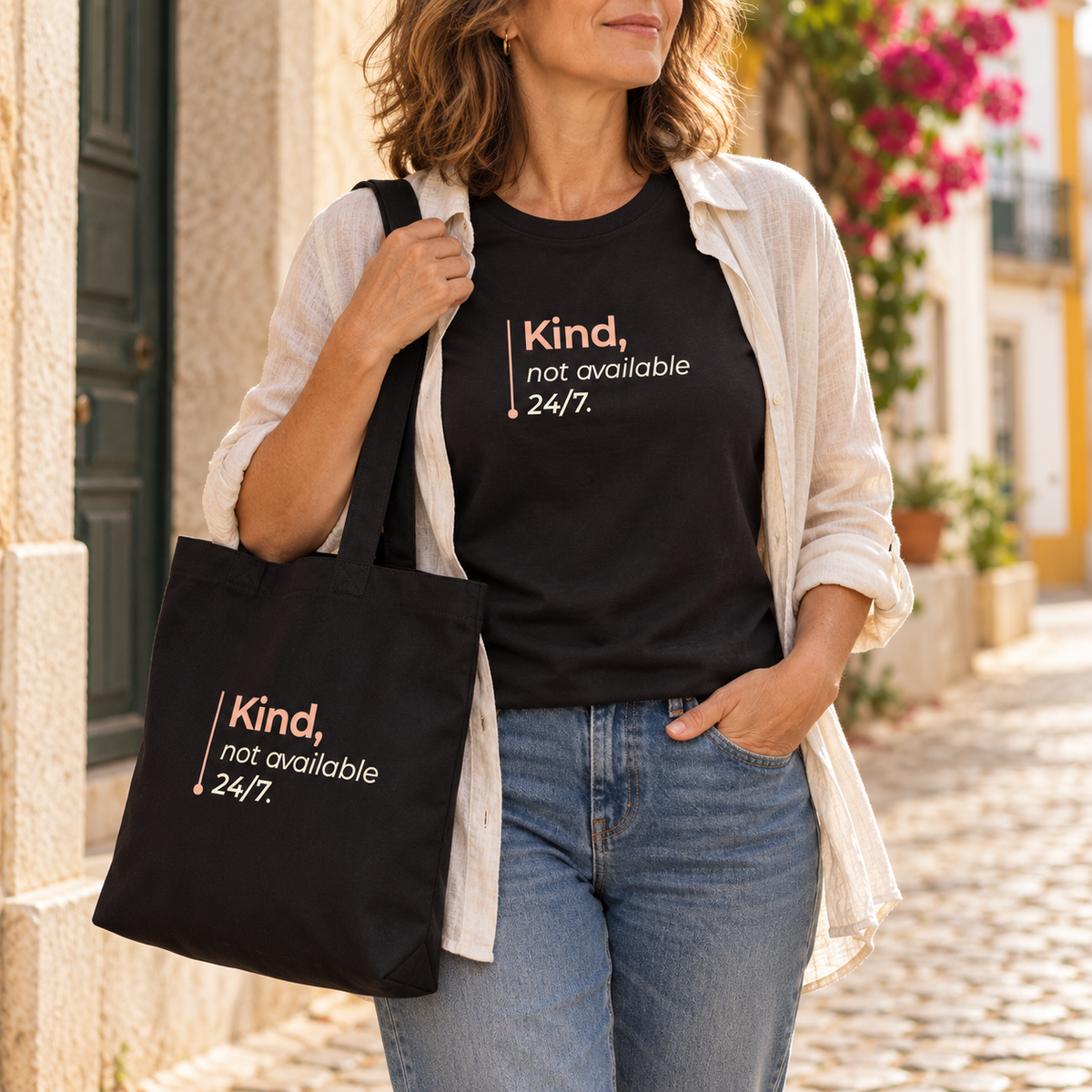 Mulher com t-shirt e tote bag pretas “Kind, not available 24/7.”, camisa clara e jeans numa rua; imagem gerada com estética UGC.