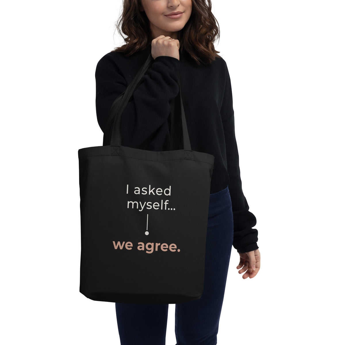 Mulher com camisola preta e jeans a segurar a tote bag preta Tag&Get com a frase “I asked myself... we agree.” em tons claros e pêssego.