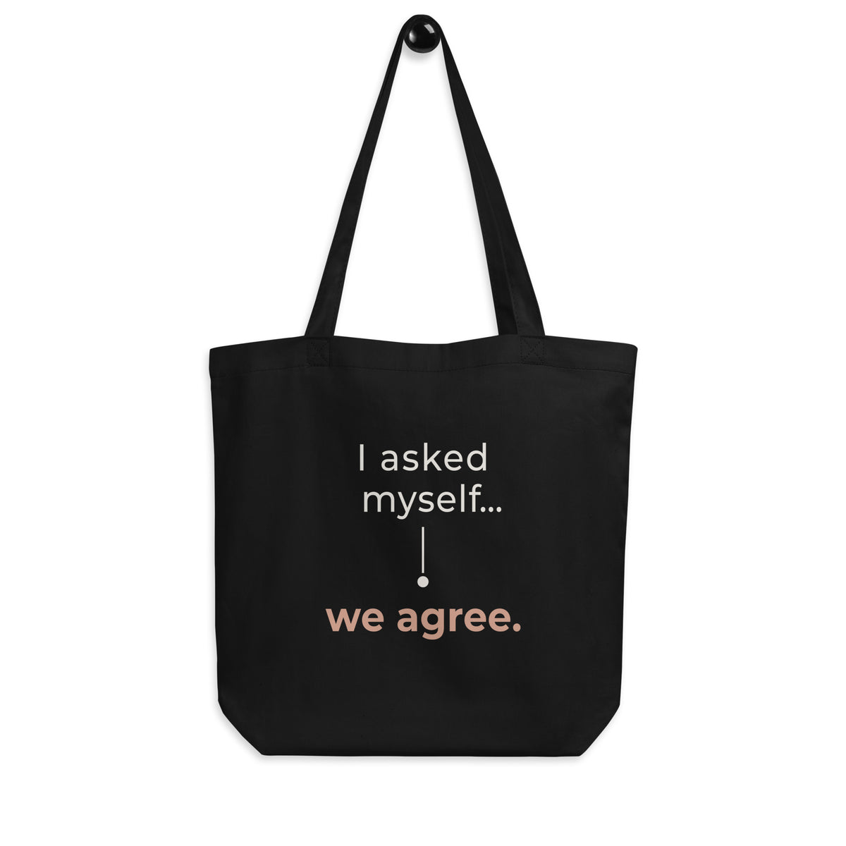 A tote bag preta Tag&Get com a frase “I asked myself... we agree.” em tons claros e pêssego, pendurada pelas alças num gancho sobre fundo branco.