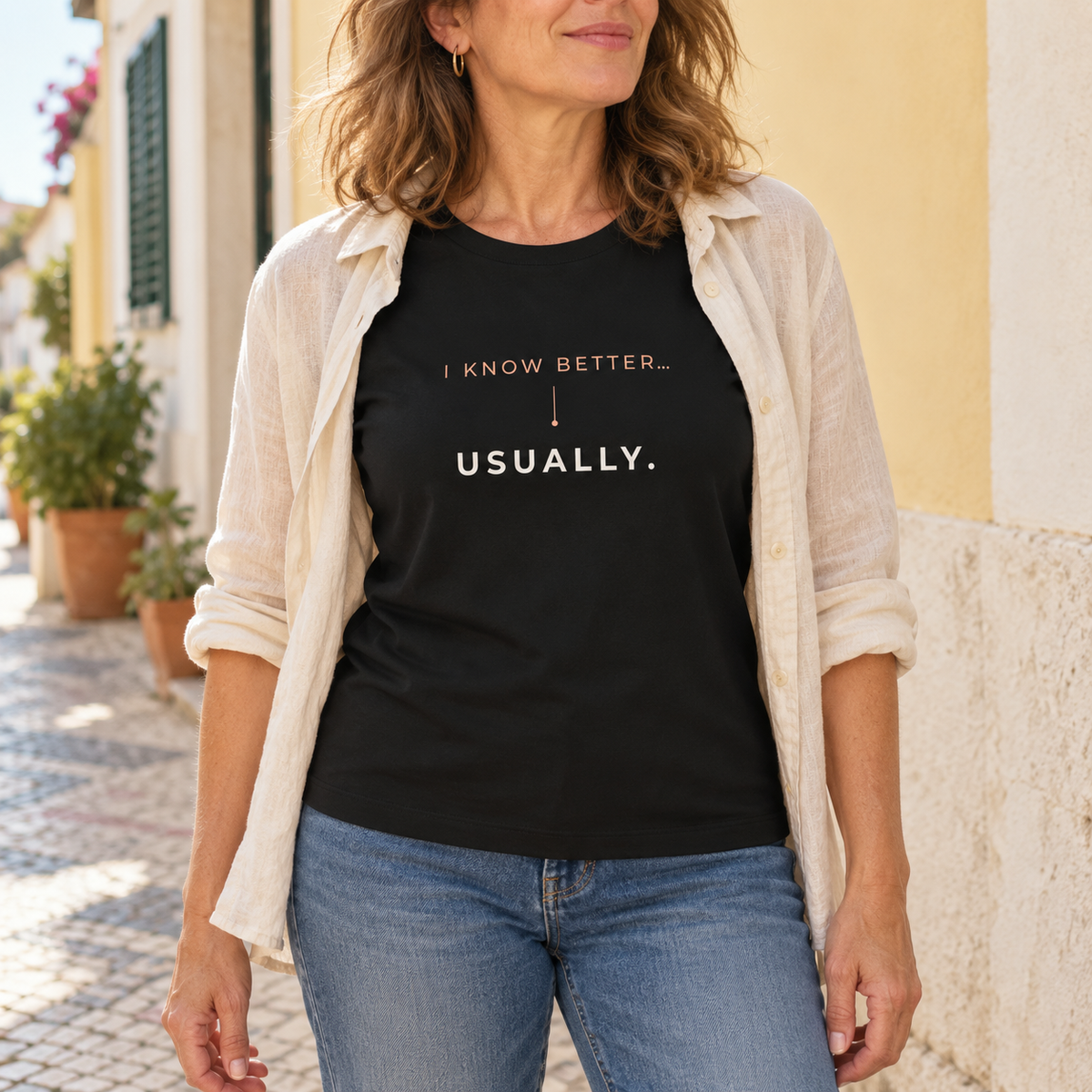 Mulher com a T-shirt preta “I know better... usually.”, camisa clara aberta e jeans numa rua portuguesa; imagem gerada com estética UGC.
