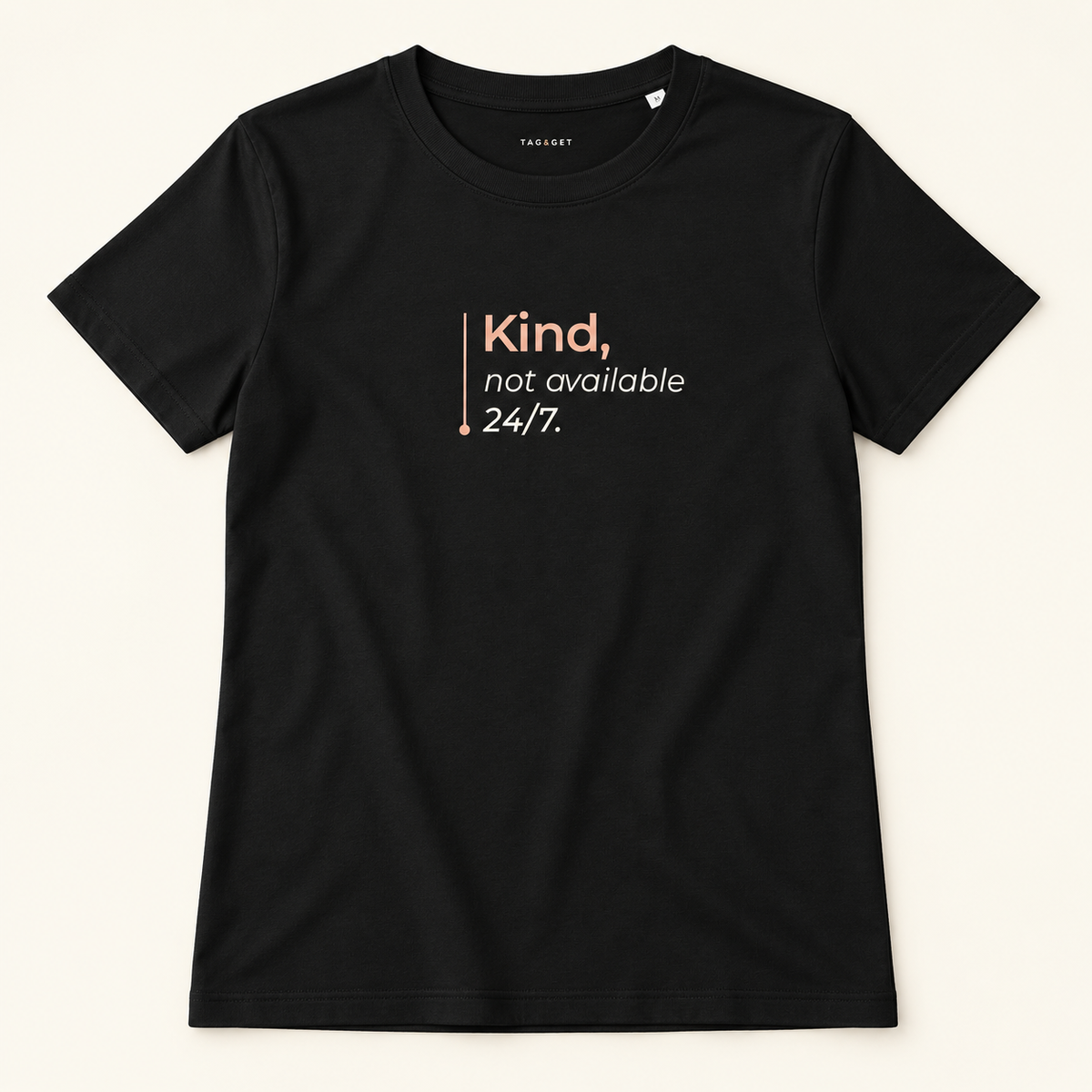 T-shirt preta Tag&Get com a frase “Kind, not available 24/7.”, vista de frente sobre fundo creme.