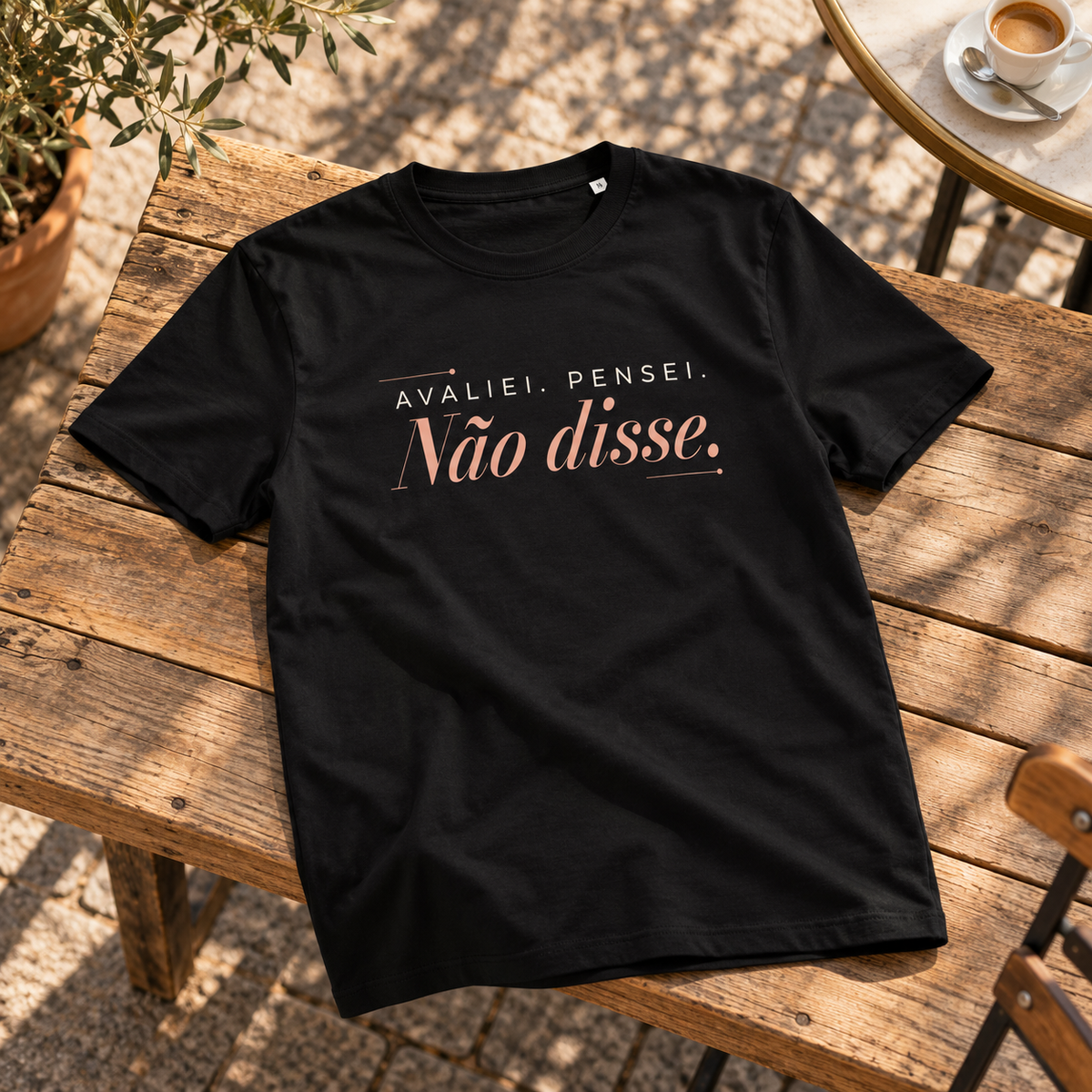 T-shirt preta Avaliei. Pensei. Não disse. estendida numa superfície de madeira numa esplanada, com estampado visível.