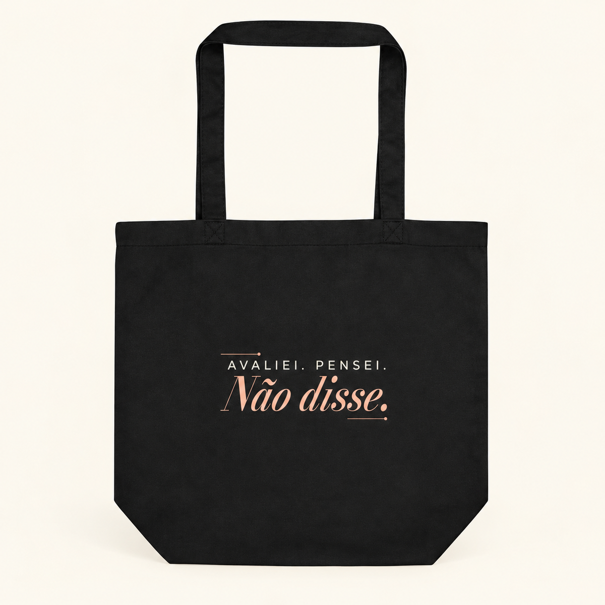 Tote bag preta com a frase “Avaliei. Pensei. Não disse.”, vista de frente e completa sobre fundo creme.