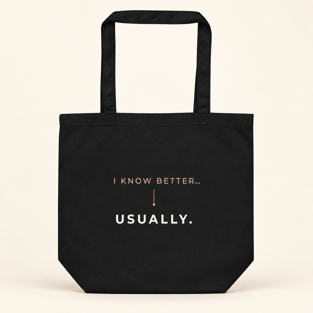 Tote bag preta com a frase “I know better... usually.”, vista de frente sobre fundo creme.
