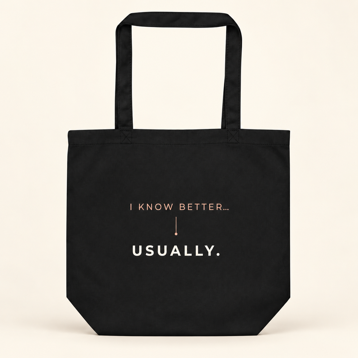 Tote bag preta com a frase “I know better... usually.”, vista de frente sobre fundo creme.