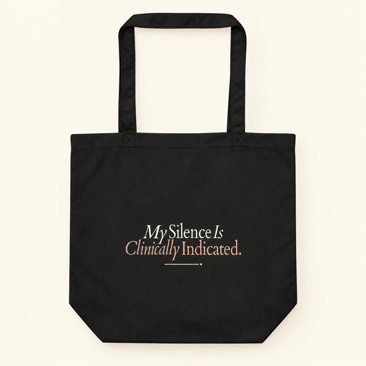 Tote bag preta com a frase “My Silence Is Clinically Indicated.”, vista de frente e completa sobre fundo creme.