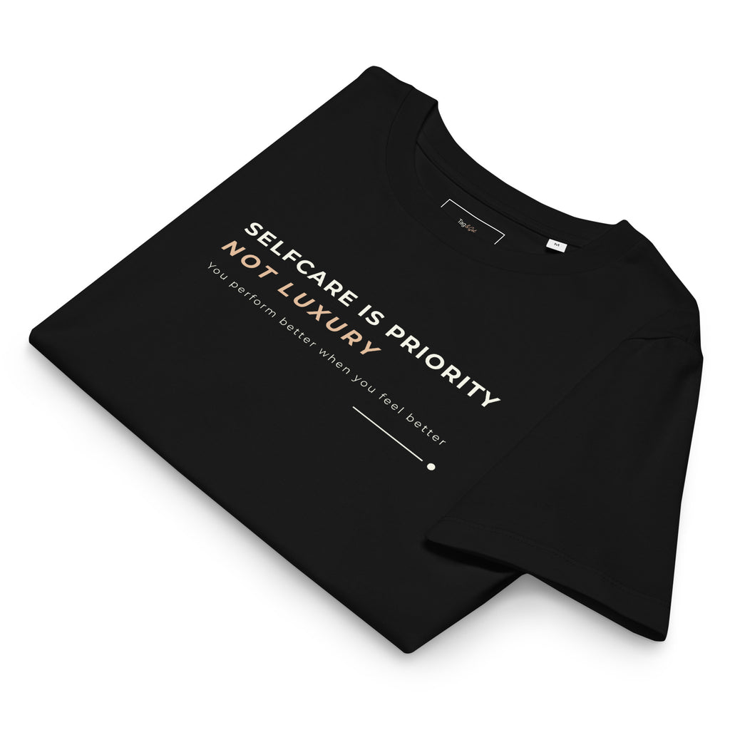 T-shirt preta dobrada com o estampado «Selfcare is priority, not luxury» visível.